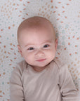 Close-up of baby smiling on the Good Life fitted sheet in cream with vegetable prints, blending warmth and whimsical character