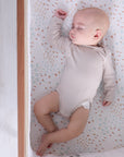 Overhead view of baby sleeping peacefully on the Good Life bedside crib fitted sheet in soft cream with vegetable garden print