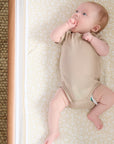Overhead view of baby lying on the Love Cats fitted sheet in beige with delicate cat print, styled in a cosy bedside crib.
