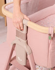 Detail view of the CoZee Air 2 bedside crib in blush height adjustment mechanism, highlighting easy one-hand adjustment for bedside positioning.