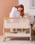 Front view of the CoZee Air 2 bedside crib in toasted oak/sand with breathable mesh panel for airflow and visibility.