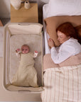 Overhead view of baby sleeping next to parent in the CoZee Zen bedside crib, illustrating closeness, comfort and safe sleep design.
