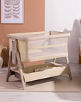 CoZee Zen bedside crib in sand with breathable mesh sides and under-crib storage shelf, styled in a calm neutral bedroom.