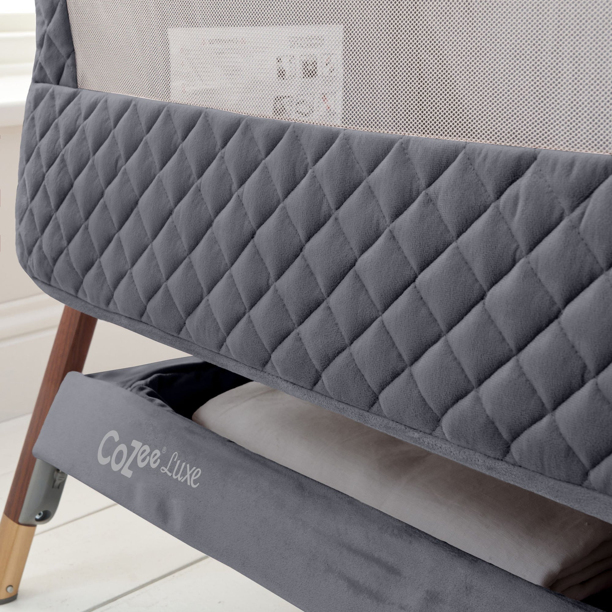 CoZee Luxe Bedside Crib in Walnut and Slate featuring a premium quilted fabric with breathable mesh sides and spacious storage shelf for baby essentials