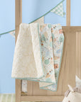 Good Life cot bed coverlet draped over cot rail, featuring reversible woodland and neutral stripe prints with soft green edging