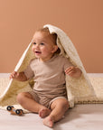 Smiling baby playing under the Love Cats cot bed coverlet, wrapped in soft quilted layers with a charming neutral animal pattern