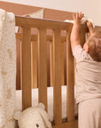 Love Cats cot bed coverlet draped over wooden cot rail, showcasing reversible leopard print design in soothing neutral tones