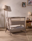 CoZee Sense bedside crib in soft walnut and cocoa finish with mesh side panel and integrated storage shelf below.