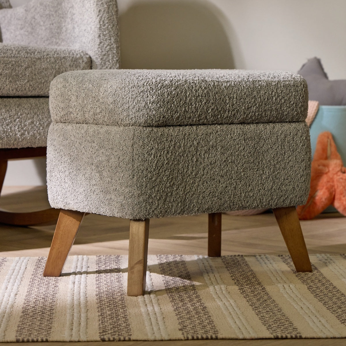 Detail of the Harper footstool in boucle cloud grey with tapered wood legs, shown in a nursery setting beside the matching chair.