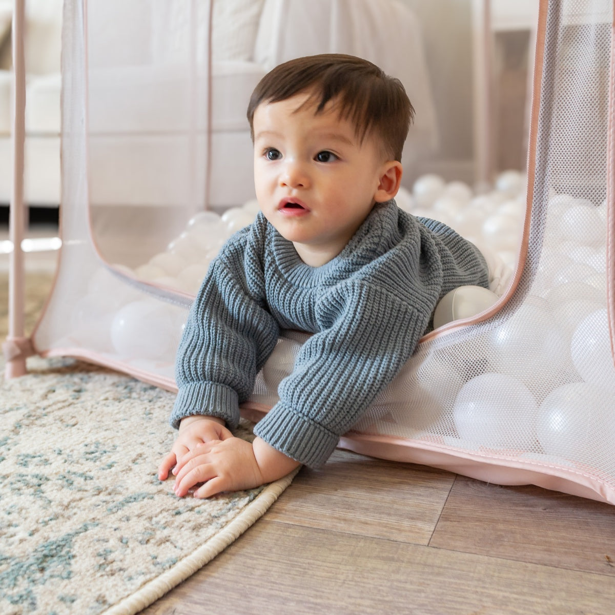 Baby crawling out of the Hexa Playpen in Gumdrop Terrazzo through the zipped opening, surrounded by soft mesh and ball pit base