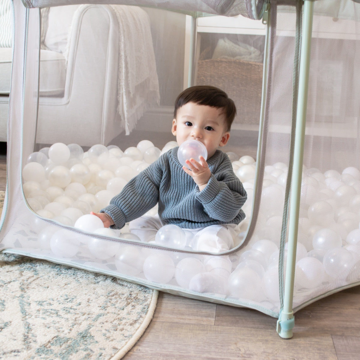 Child holding a clear ball inside the Hexa playpen in Leaf Terrazzo, featuring breathable mesh and soft padded flooring
