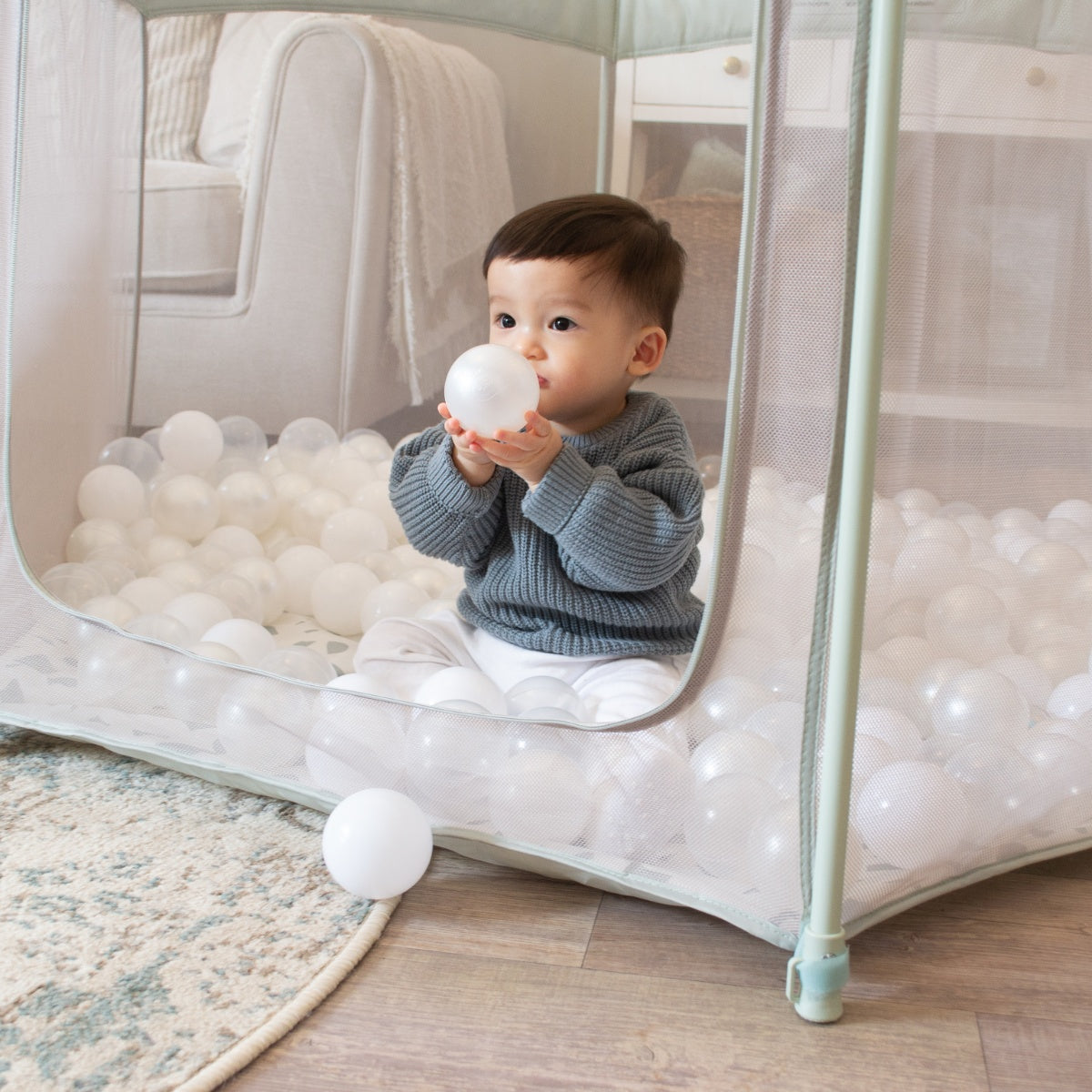 Child sitting inside the Hexa playpen in Leaf Terrazzo holding a play ball, surrounded by soft edges and cushioned flooring