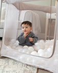 Child playing inside the Hexa Playpen in mushroom terrazzo, filled with soft white play balls and zip-down side open for easy access