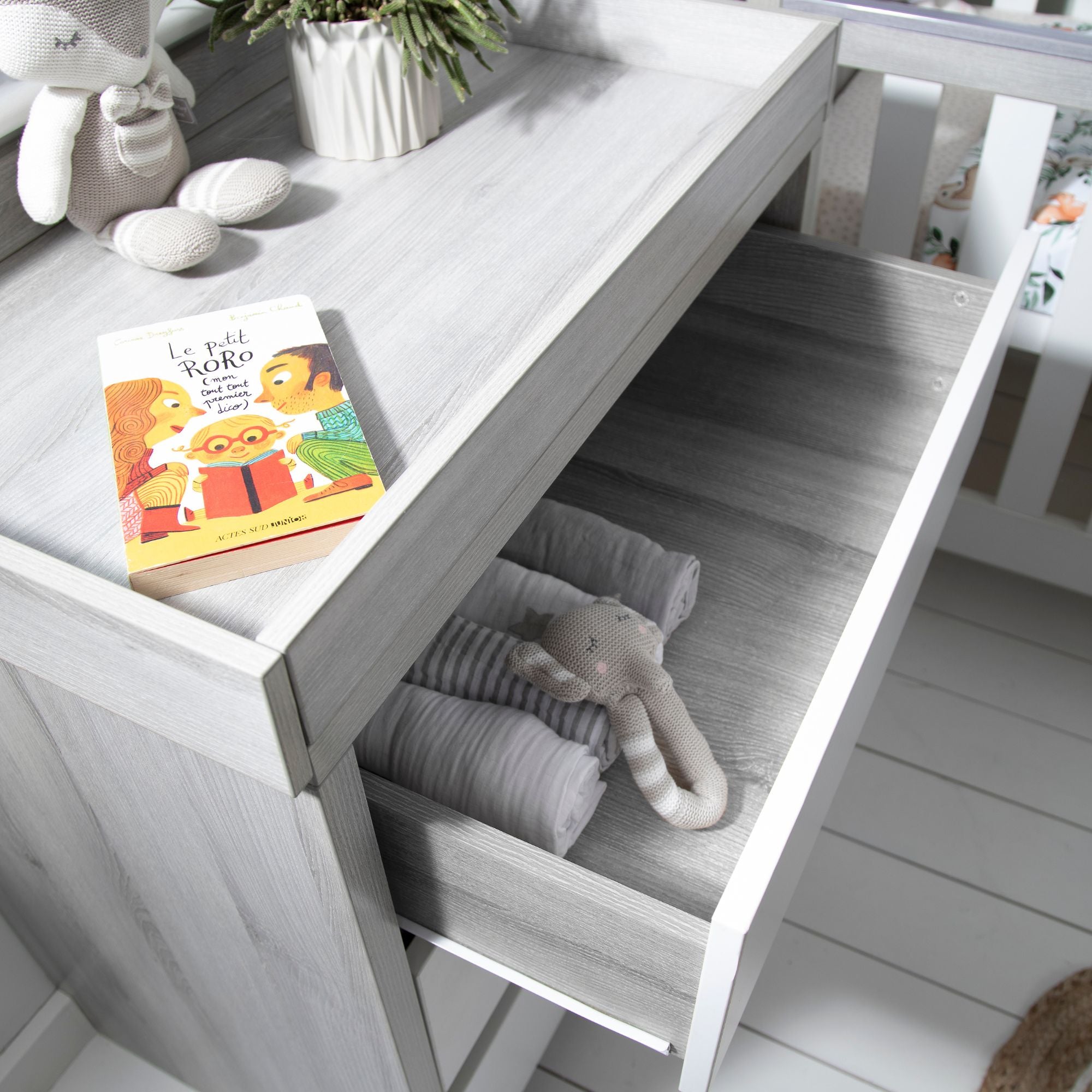 Modena chest changer in grey ash and white with open top drawer, neatly storing rolled blankets and a soft toy, highlighting practical nursery storage