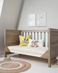 Modena Cot Bed in White and Oak shown in sofa bed mode with bedding, cushions, and soft toys, perfect for a modern nursery setting.