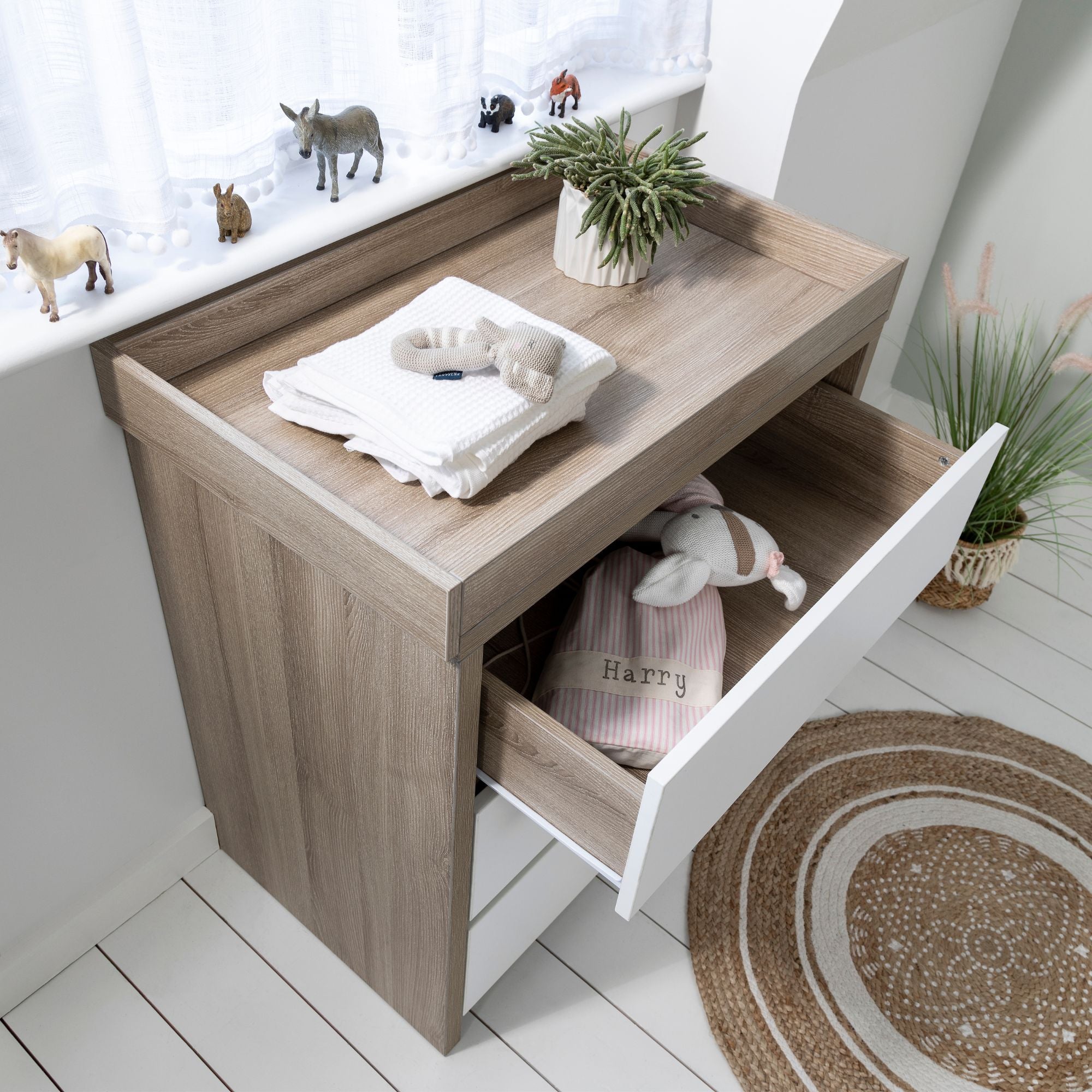 Modena Chest Changer in White Oak shown with open drawer, displaying neatly organized baby essentials and toys, perfect for creating a functional and stylish nursery space.