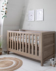 Lifestyle image of Modena Cot Bed in Oak styled in a nursery, featuring woodland print bedding and modern decor accents