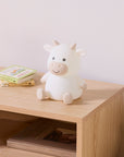 White and brown cow night light on a wooden surface with books in the background