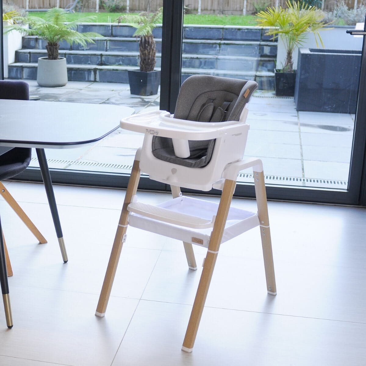 Lifestyle view of Nova evolutionary highchair in white/oak set by a dining table, showcasing the modern design, adjustable tray, and storage basket.
