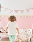 Child walking towards toddler bed styled with pink floral bedding and tiny tails nursery bunting in a soft blush bedroom.
