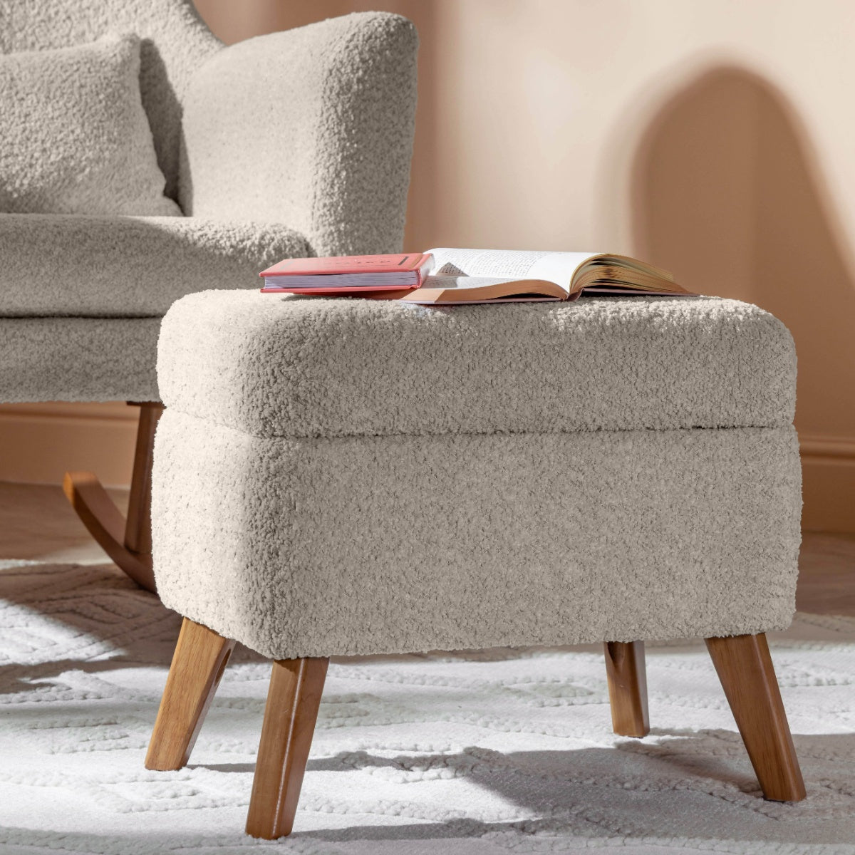 Lifestyle close-up of the Oscar Luxe footstool in sage boucle with books on top, styled beside the matching rocking chair on a pale rug.