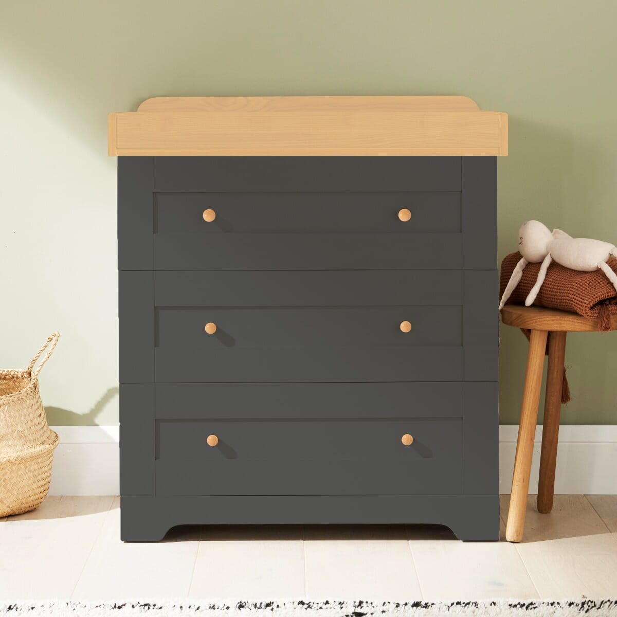 Lifestyle front view of the Rio chest changer in Honey Oak and Slate Grey, featuring three spacious drawers, a removable top changer, and round wooden handles for a modern nursery look
