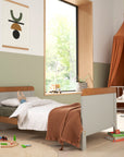 Rio cot bed in dove grey converted to a toddler bed, styled in a modern nursery. The honey oak accents add warmth to the space, while the open sides provide easy access for toddlers transitioning from cot to bed.