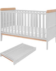 Rio cot bed in dove grey with warm honey oak trim, shown with a separate coordinating changing top. Features fixed rails and a spacious underbed area, ideal for combining with underbed storage.