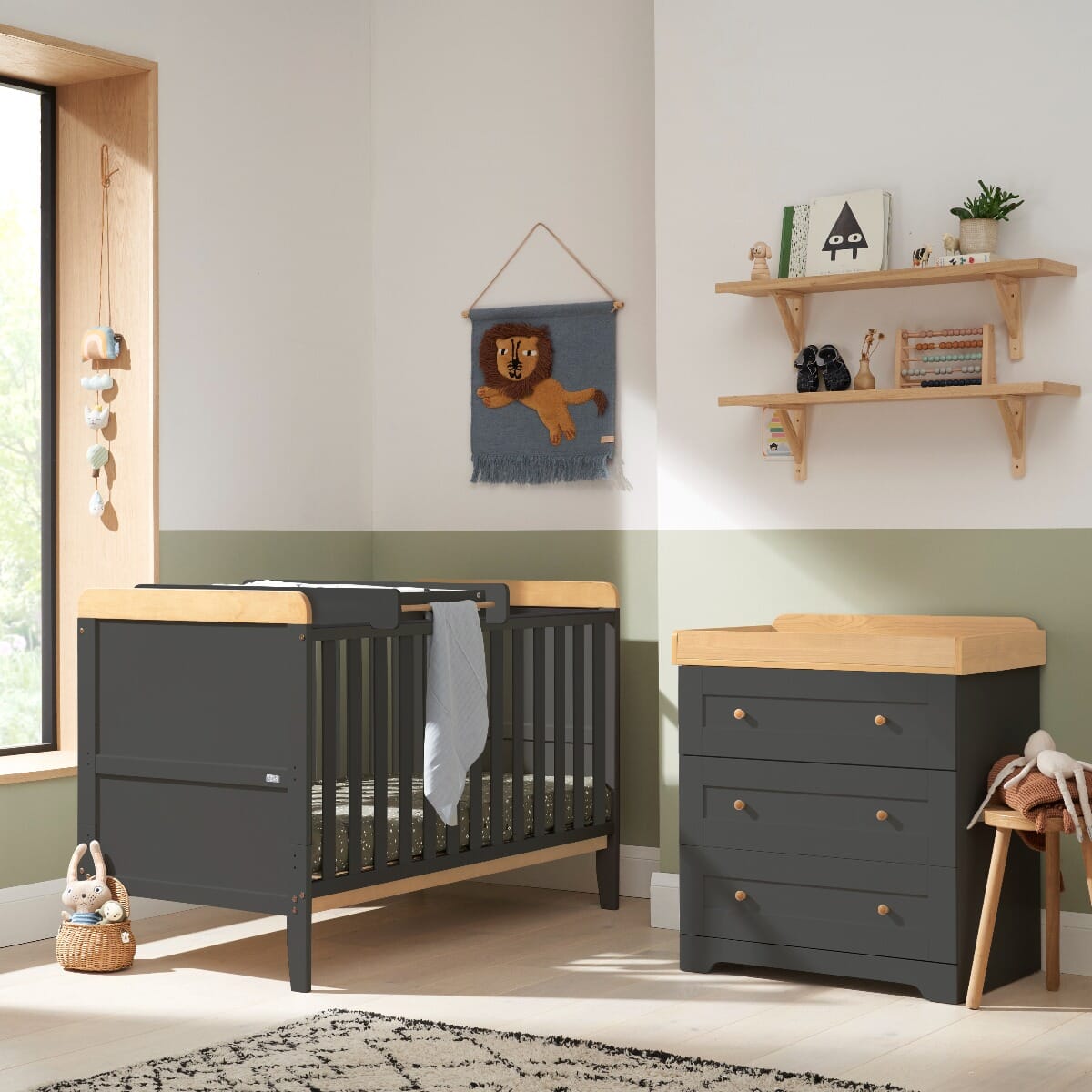Styled nursery room featuring the Rio cot bed and chest changer in slate grey and honey oak, with modern decor, natural light, and functional storage and sleeping space for baby.