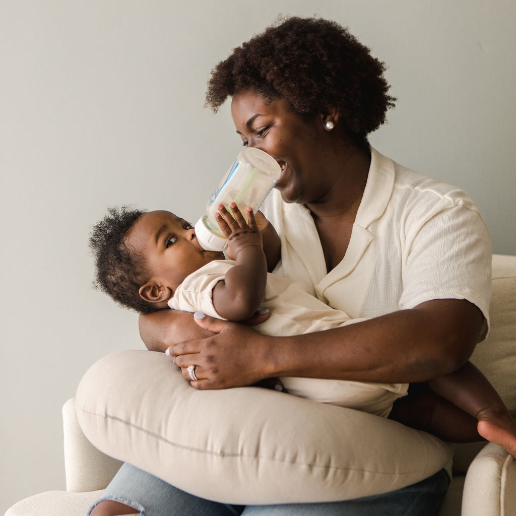 Baby being bottle-fed while resting on SMO nursing pillow in birch, showing cosy support and relaxed bonding time