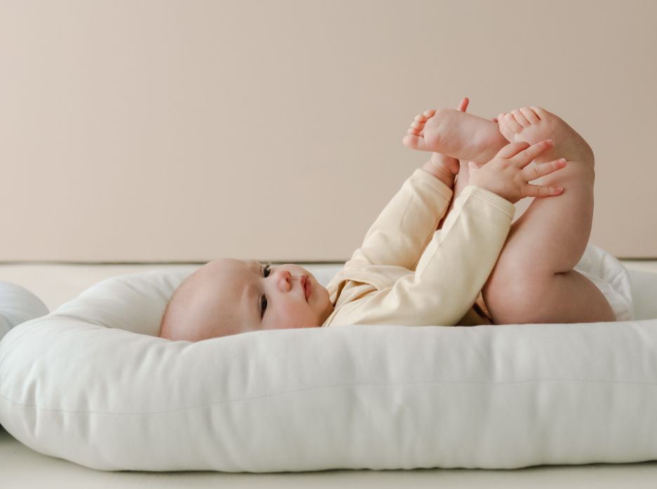 Baby resting on a newborn lounger, cradled in a supportive, cocoon-like shape for a comforting held sensation.