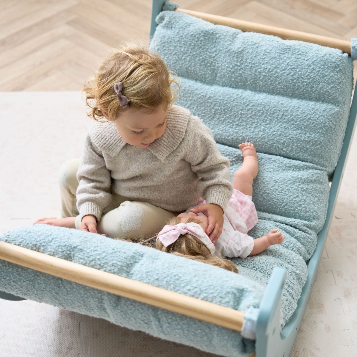 Top-down view of toddler playing gently with a soft toy doll on the ocean stone cushion
