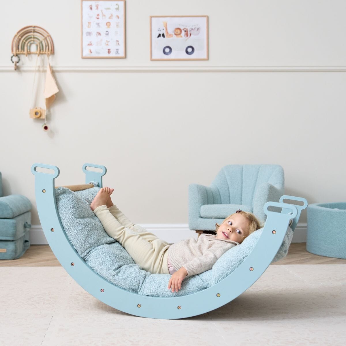 Toddler relaxing back on the Scala Montessori Pikler rocking frame with ocean stone cushion, showing its soft comfort and full-body support