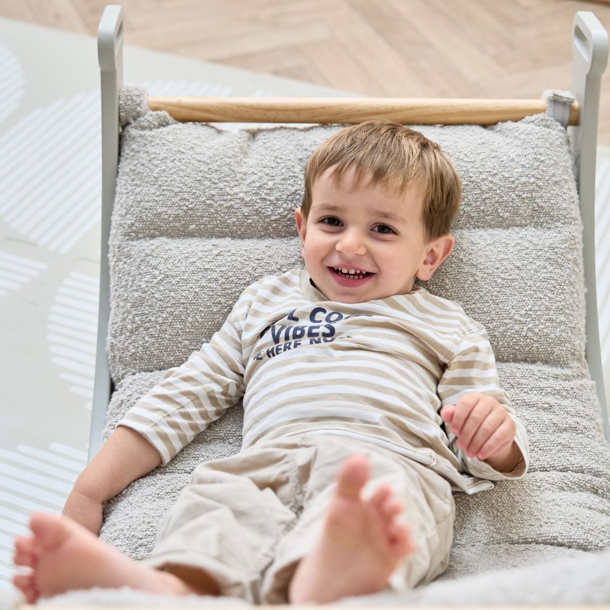 Close-up of smiling toddler reclining on the Scala Montessori Pikler cushion in Boucle Mushroom, showing plush support and secure positioning