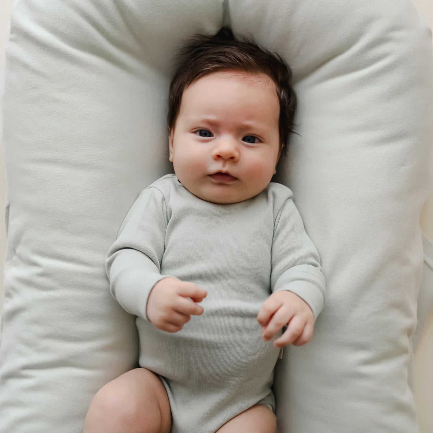 Baby rests in snuggle me lounger cover sage β soft fabric adds comfort while cradling baby in a calming, ergonomic shape.