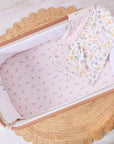 Baby crib with pink crib sheet and floral blanket on a light wooden floor.