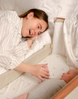 CoZee Air Bedside Crib in Scandinavian Walnut/Ecru - lifestyle image with mother and baby, crib attached to the bed