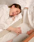 CoZee Air Bedside Crib in Scandinavian Walnut/Ecru - lifestyle image with mother and baby, crib attached to the bed
