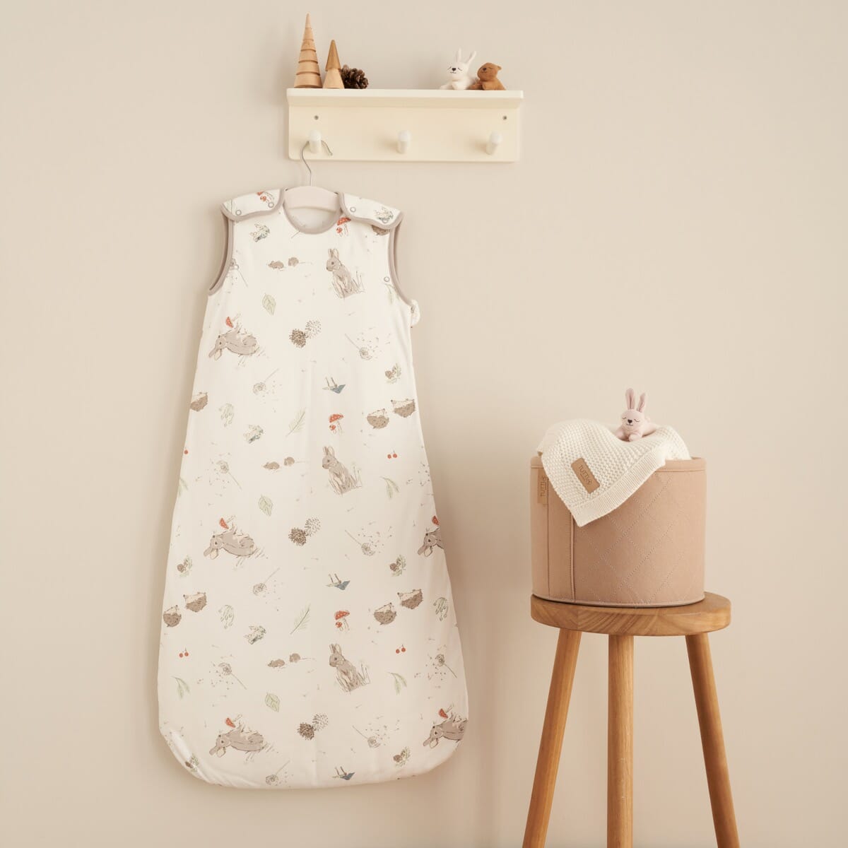 Cocoon print baby sleep bag 0-6 months hanging on nursery peg rail beside toys, creating a cosy, woodland-themed sleep space.