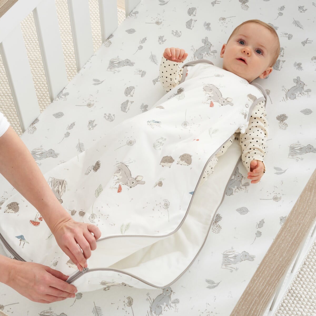 Parent zipping baby into the Cocoon baby sleep bag 6–18 months, showing practical side zip and calming woodland design for bedtime ease