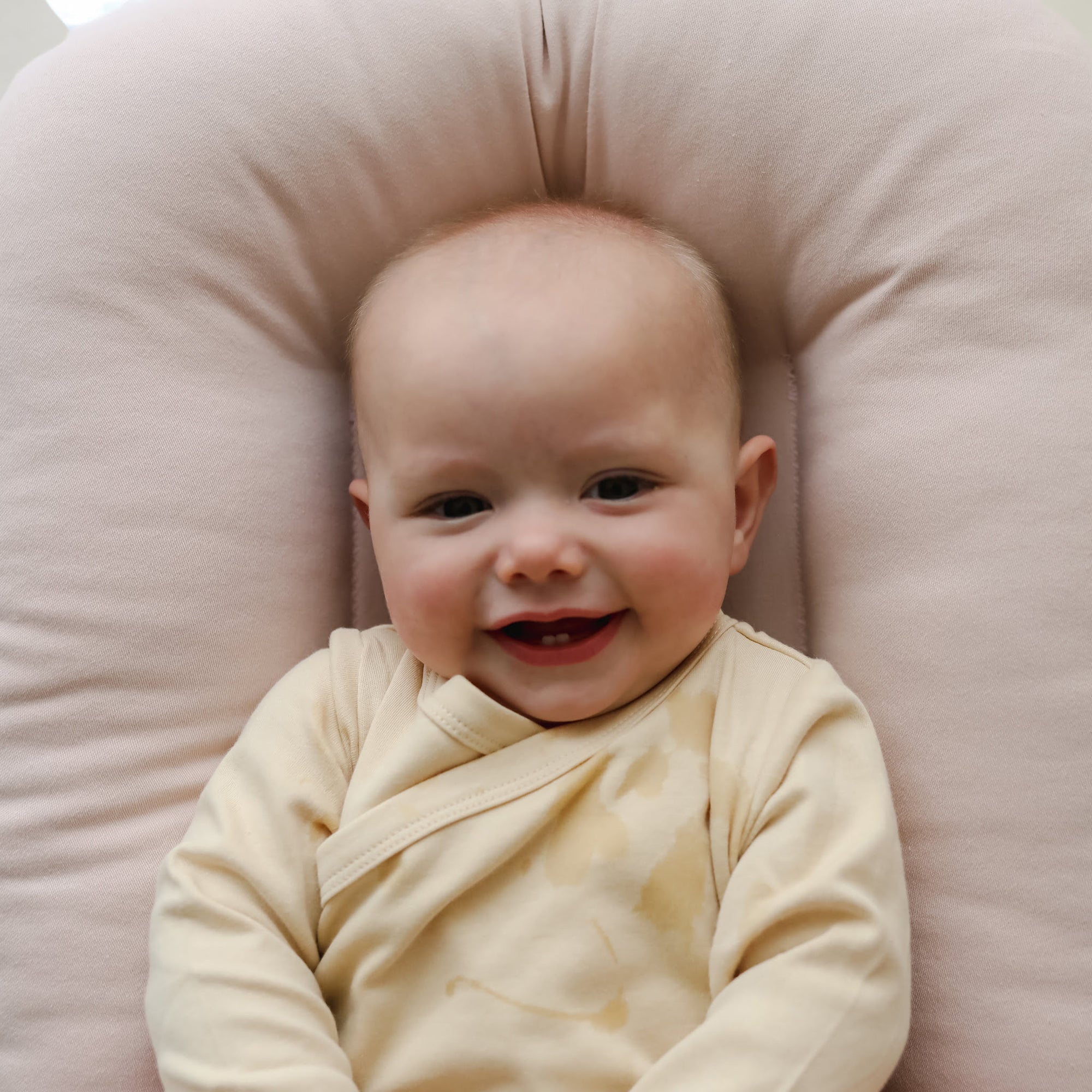 Smiling baby lying in the Snuggle Me Newborn Lounger in Petal, showing soft contoured nest design and happy lounging moment