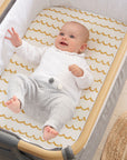 Baby lying in crib on Our Planet fitted sheet with mustard wave pattern, highlighting breathable organic cotton fabric and cosy design