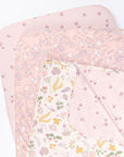Cutout view of the Tiny Tails bedside crib starter pack featuring two floral pink fitted sheets and a reversible coverlet