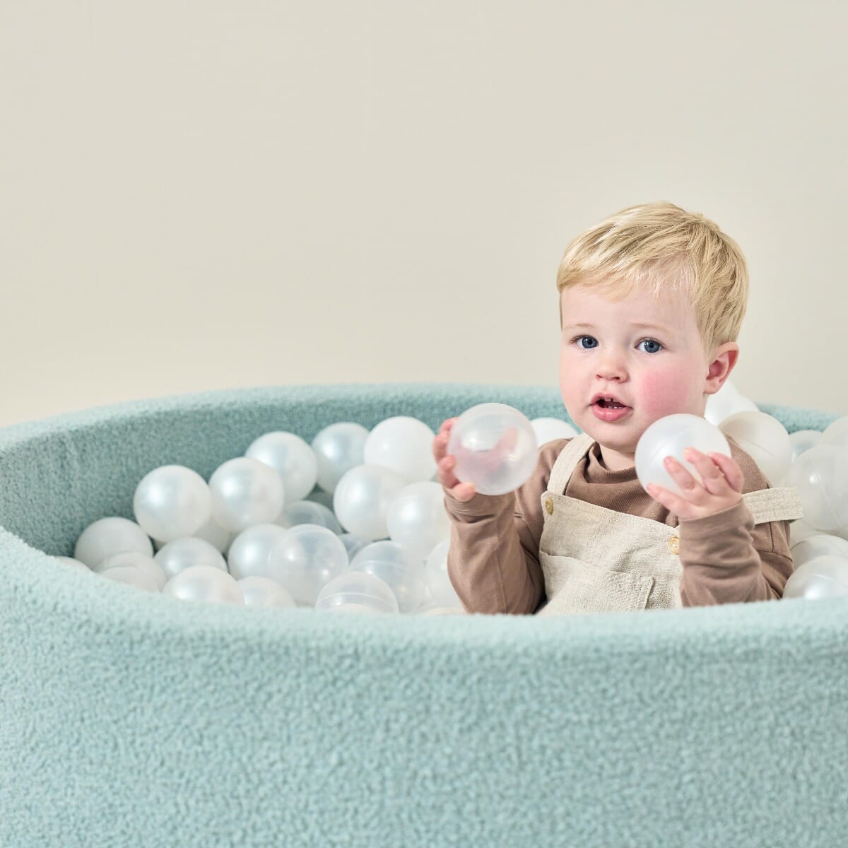 Bola Baby Ball Pit in Ocean Stone - lifestyle image of little boy playing and grabbing into some of the ball pit balls