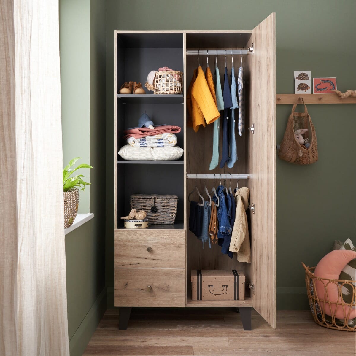 Open door view of the Como wardrobe in distressed oak and slate grey, styled with shelves, drawers, and hanging rails for organised nursery storage