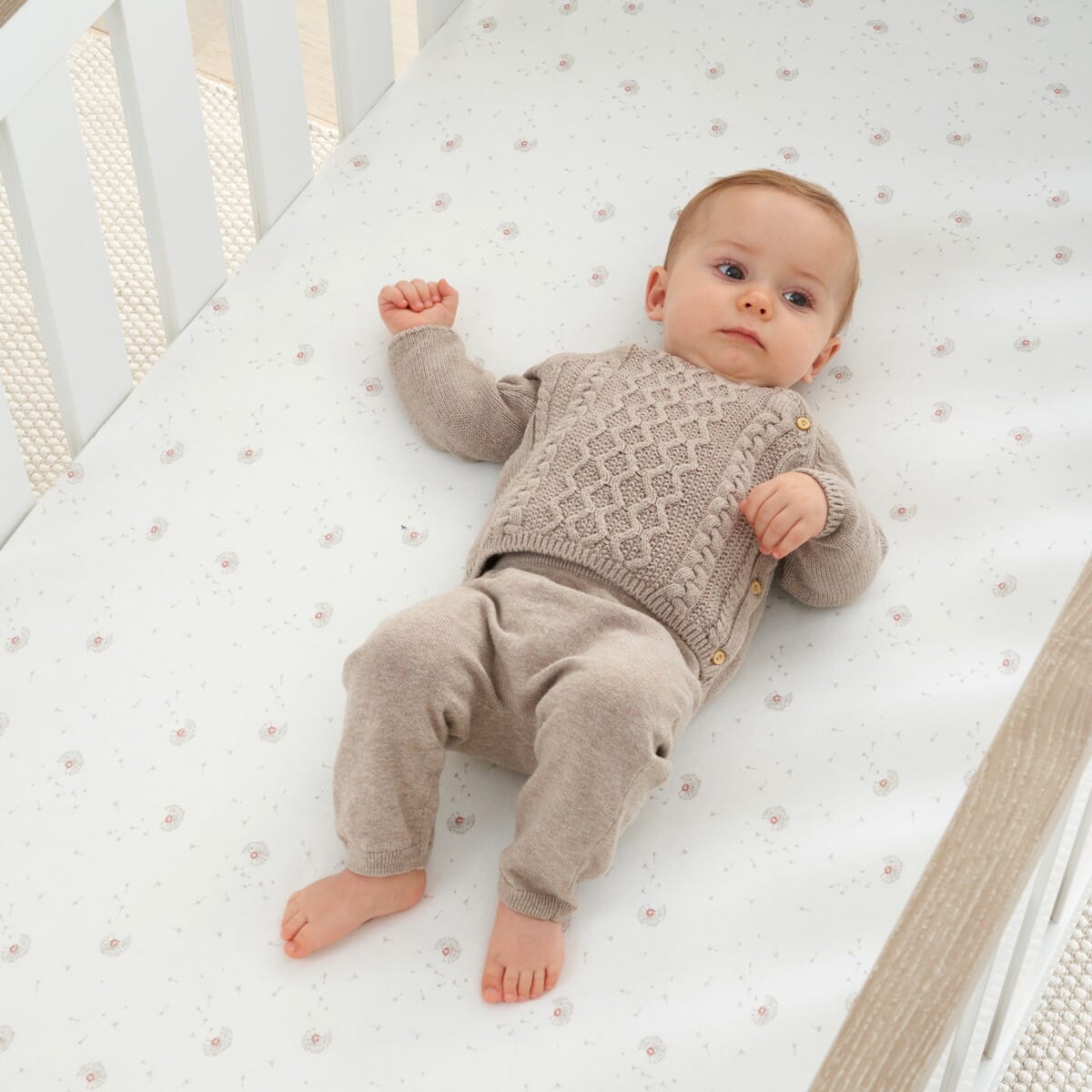 Baby resting on Cocoon cot bed fitted sheet with soft dot print, highlighting gentle organic cotton fabric for comfort and safe sleep