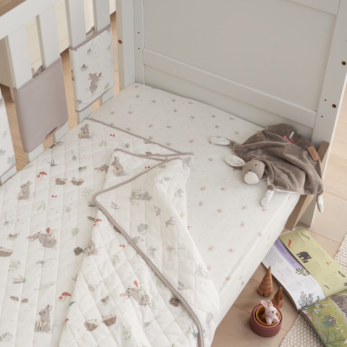 Lifestyle view of Cocoon coverlet draped over cot, soft quilted cotton with woodland prints for snug comfort and nursery style