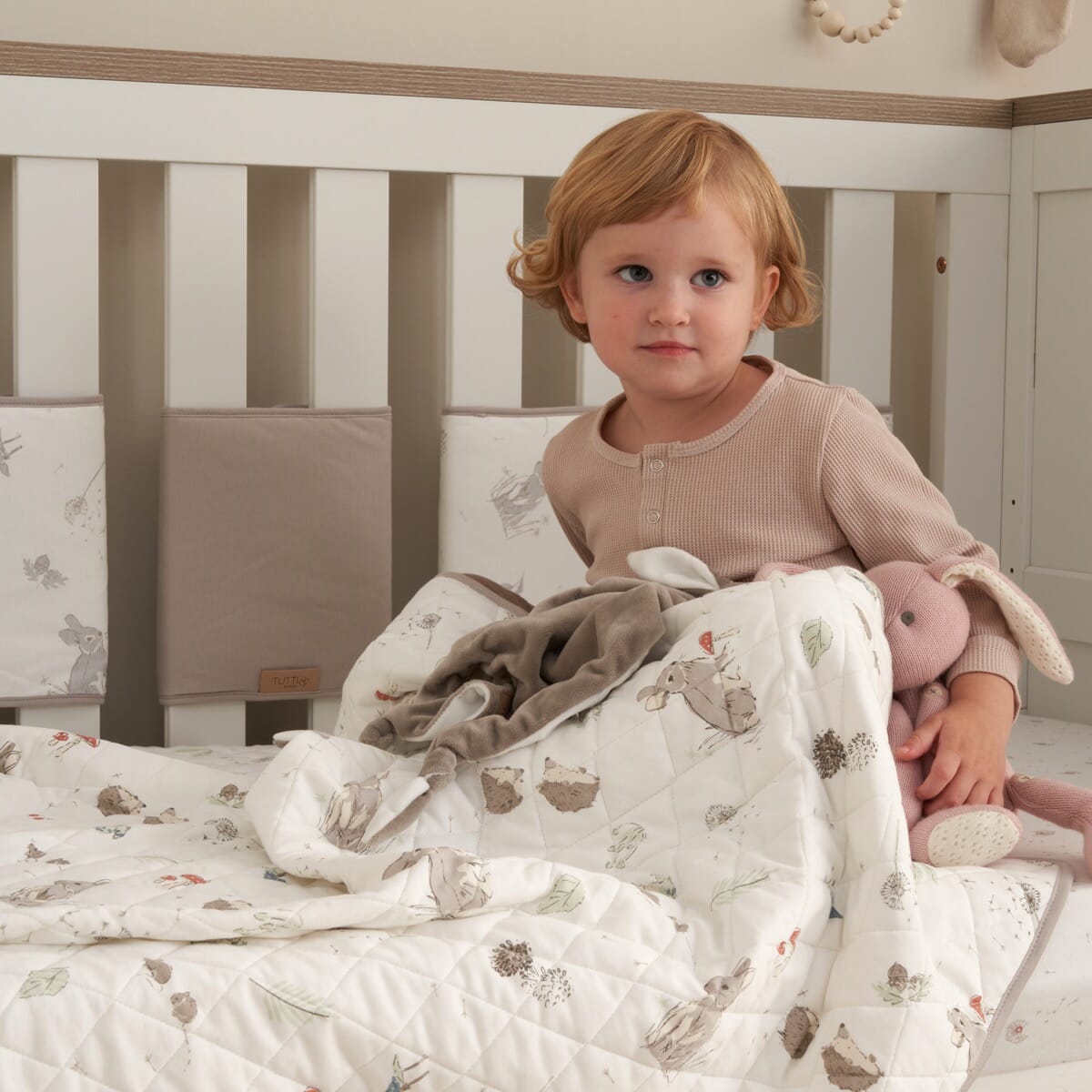 Toddler sitting with Cocoon coverlet, quilted cotton layer with woodland prints creating warmth and a calming, cosy sleep space