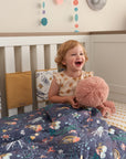 Smiling toddler with Our Planet coverlet, quilted cotton featuring ocean-inspired prints offering warmth, comfort, and playful charm