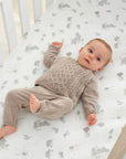 Baby lying on cot fitted sheet in Cocoon design, with woodland animal prints, providing a snug and breathable sleep surface